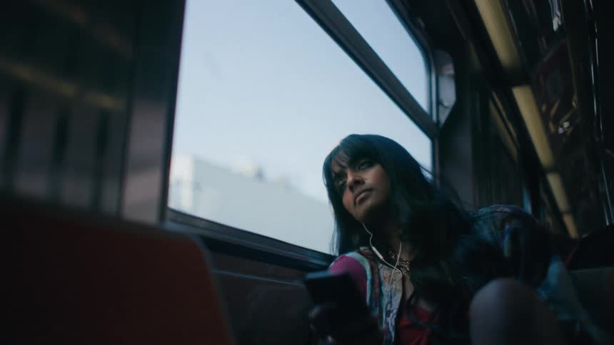 A woman sitting in a public transport vehicle and she is watching the window and then looking at her cell phone