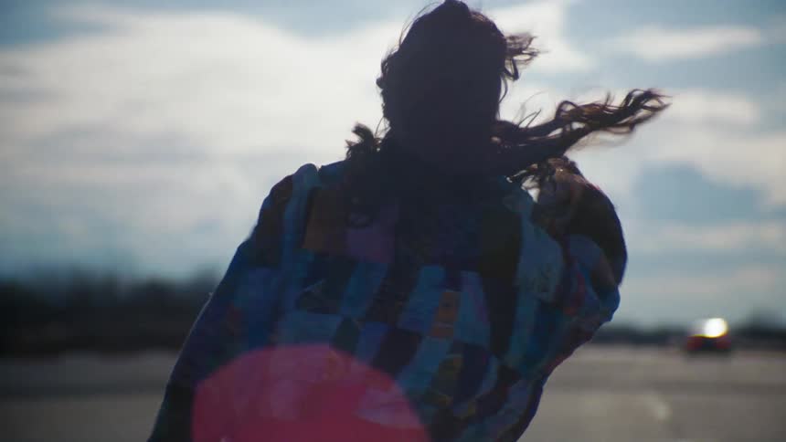 A woman with long hair wearing a colorful jacket skating at dusk