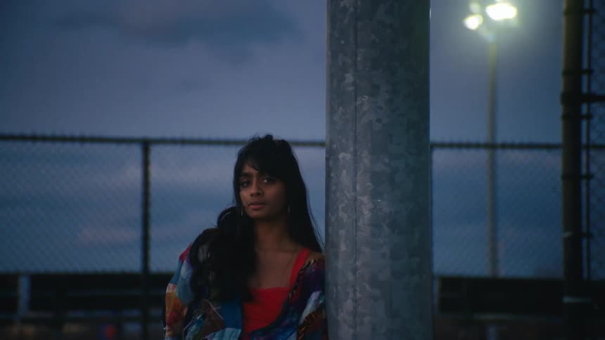 A young man and woman are leaning against a concrete post in a dusk