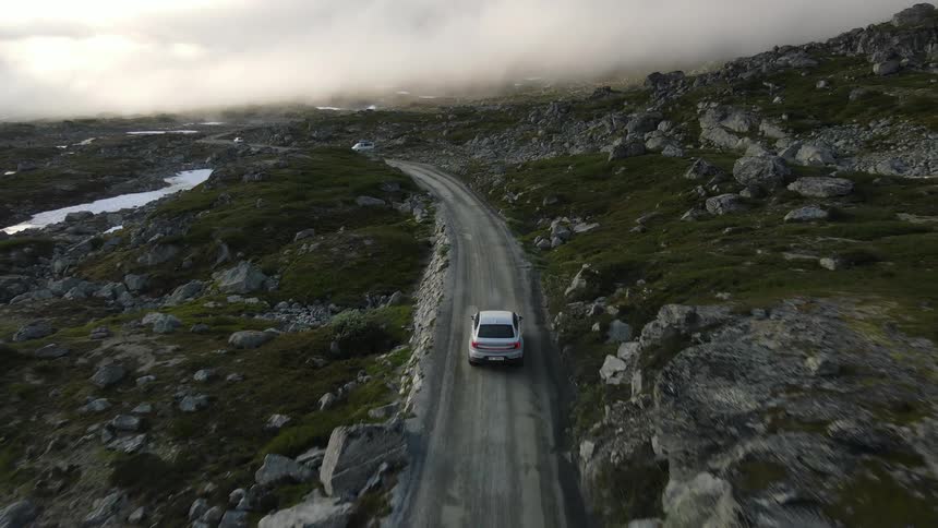Car drives along road passing frozen ponds and rocky slopes on an overcast day