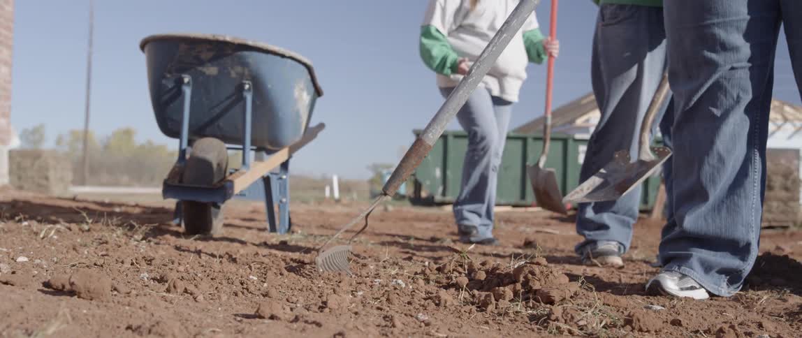 Workers rake and shovel dirt on a sunny day