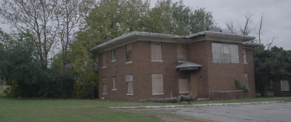 A rundown apartment building stands boarded up on an empty street
