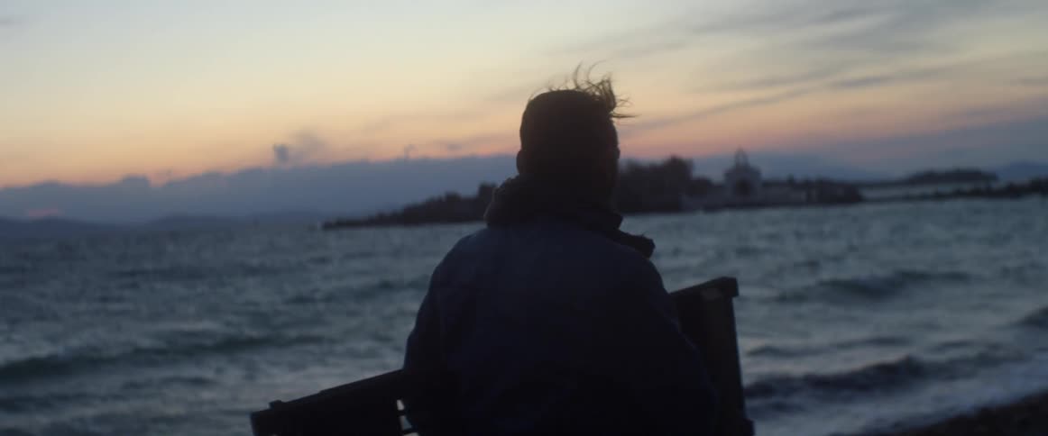 A man standing on the shoreline as waves roll in and the sun sets
