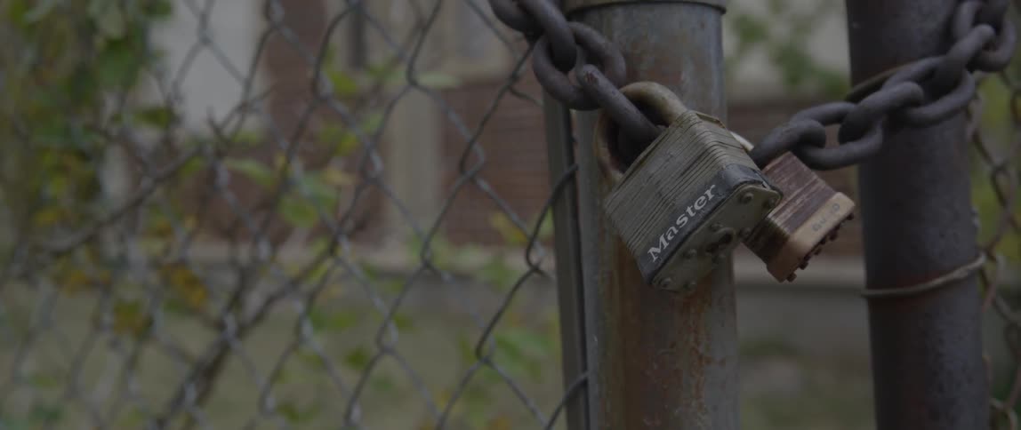 A master lock secures a thick chain on a fence