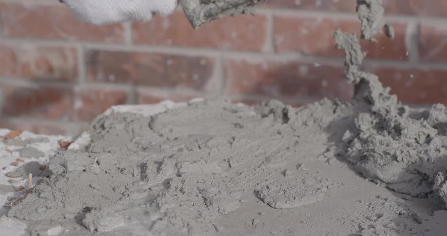 A person scoops up cement with a trowel