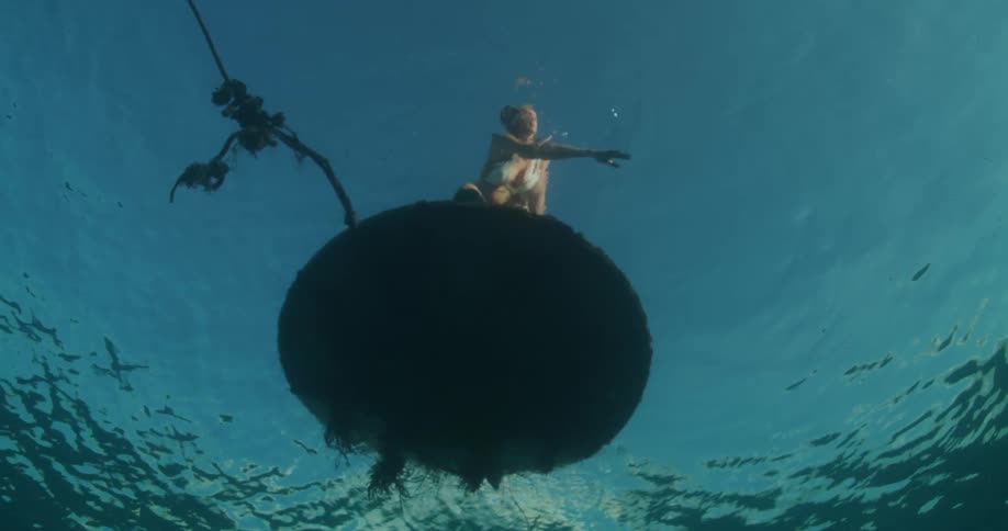 Upward view into the ocean of a woman standing on a platform running her hand through the water