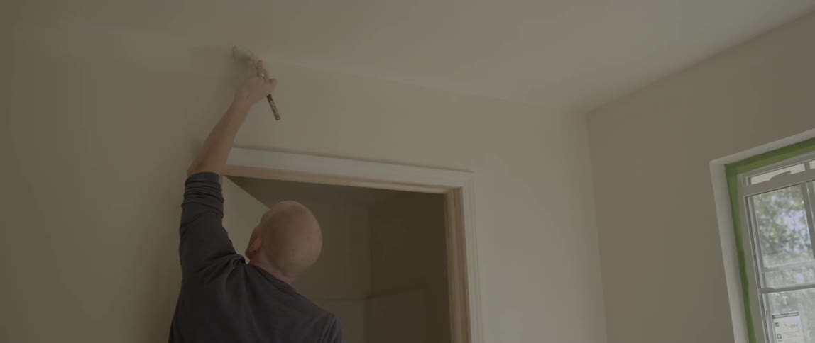 A man painting an interior room white