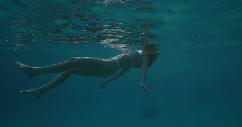 A woman wearing a swimsuit swimming underwater floating near the surface
