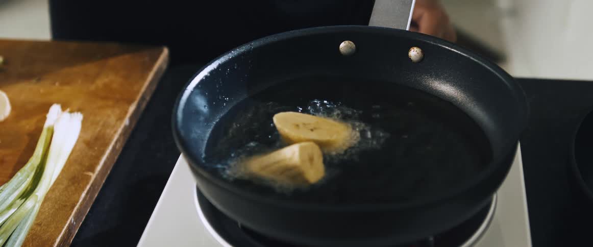 Plantain slices being placed in a frying pan with hot oil