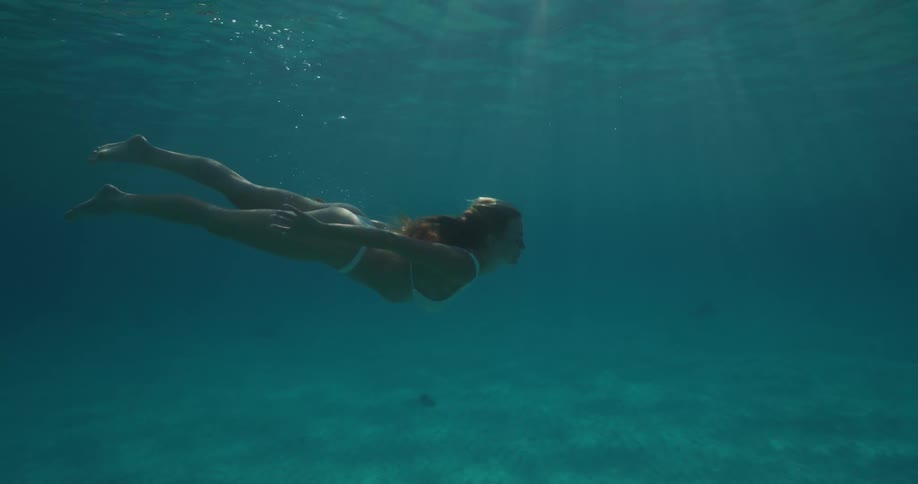 Submerged woman swimming in a blue ocean with sun rays