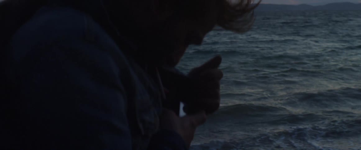 A man lights a cigarette in the wind on the beach at dusk