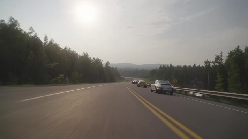 Several fast cars race down a road running through a rural area
