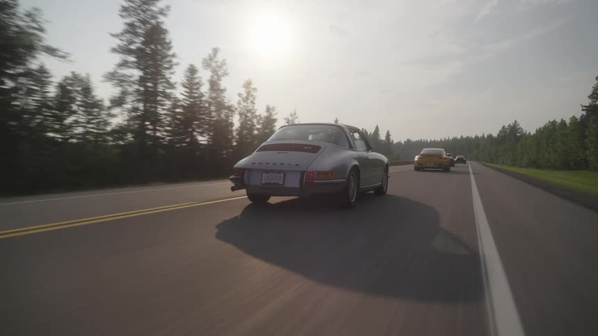 Several classic cars cruise down a scenic highway