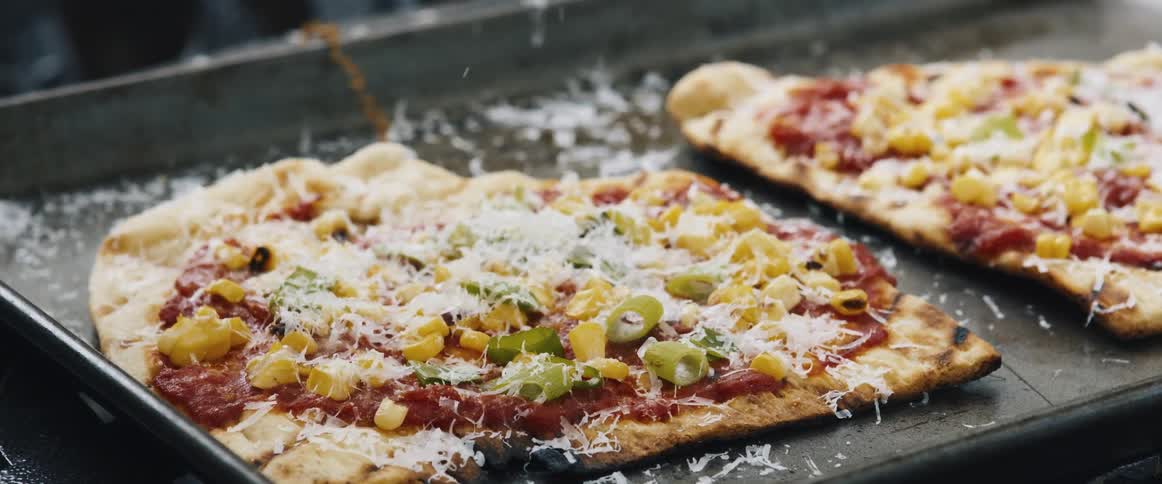 Grated cheese falling on top of a pizza being prepared