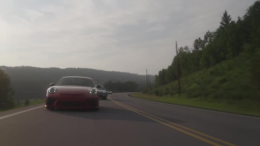 Sports cars traveling along a road with mountains and trees around
