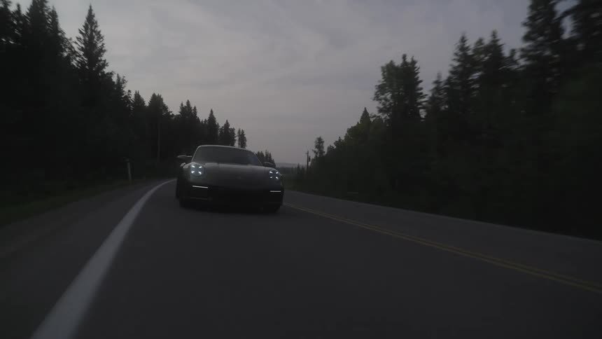 A black car driving on a twolane road surrounded by dense trees