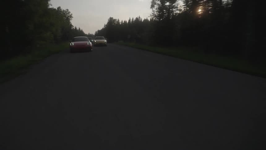 Colorful Porsches race down a highway through the forest at sunset