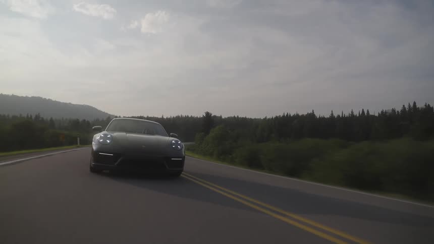 A gray Porsche 911 sports car driving on an asphalt road