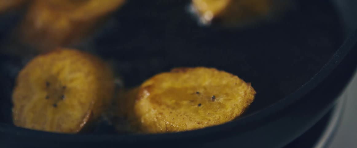 Slices of plantains being fried in a frying pan