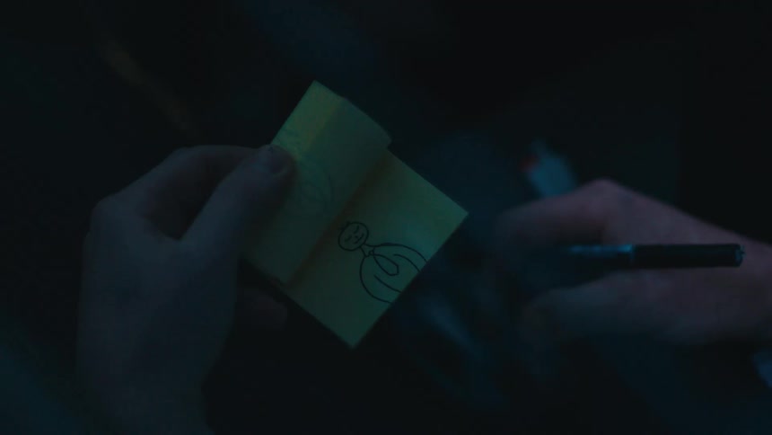 A mans hands holding a cigarette while using a pen to doodle an animation sequence on a post it pad