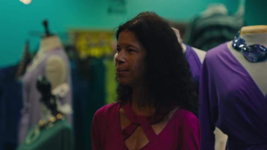A woman in a pink top is standing in front of mannequins dressed in stylish outfits appearing to be in a boutique or clothing store