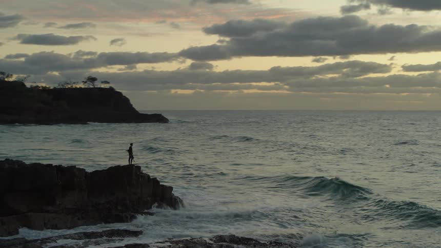 Silhouette of a person on a rocky peak on the edge of a beach one morning