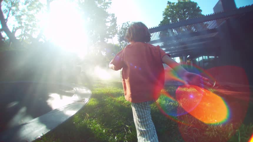 A child is running backwards in a yard with green grass