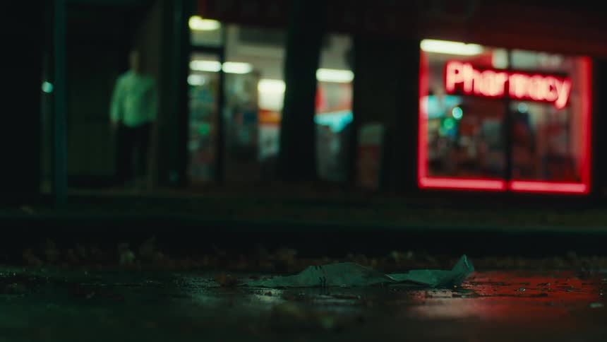 At night a man picks up a piece of litter next to a pharmacy