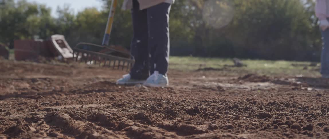 Person leveling dirt with soil rake