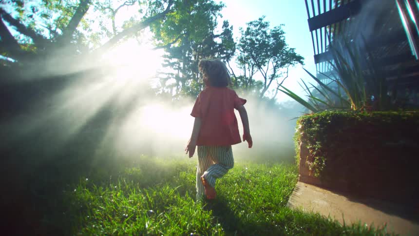 A child is on his back running in a green grass yard with strong sunlight coming from the front