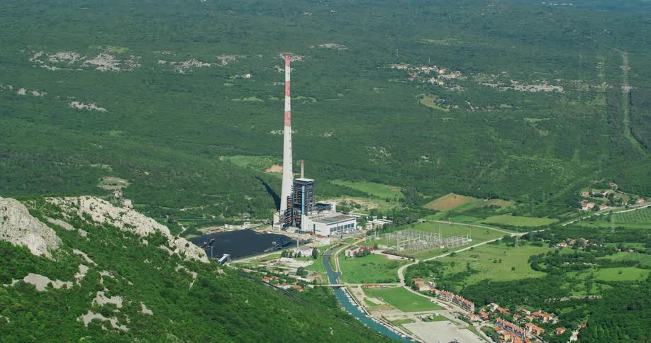 Aerial view of a coal fired power plant with smokestacks cooling towers and coal storage silos surrounded by trees