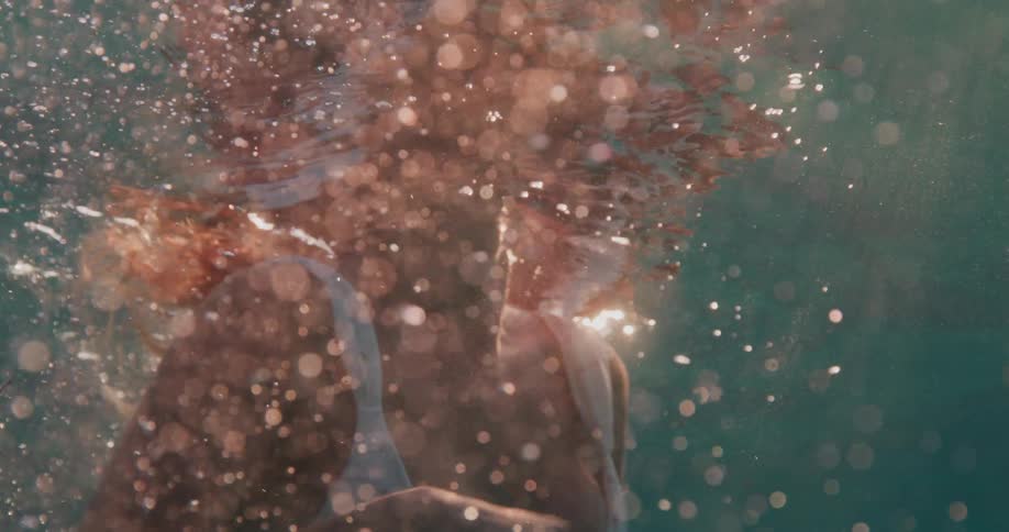 Woman swimming inside the ocean with sunlight reflection wearing a white bikini