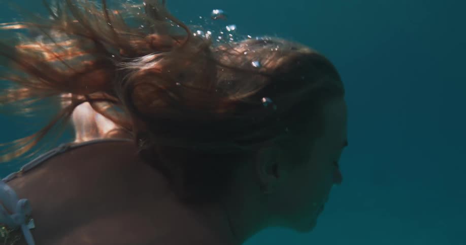 Young woman with light hair and a white bikini diving in the ocean