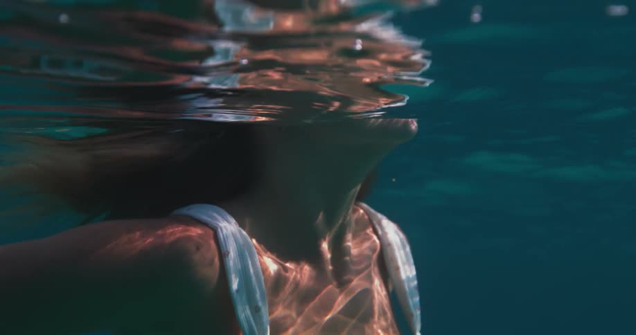 Womans body submerged in an ocean wearing a white bikini