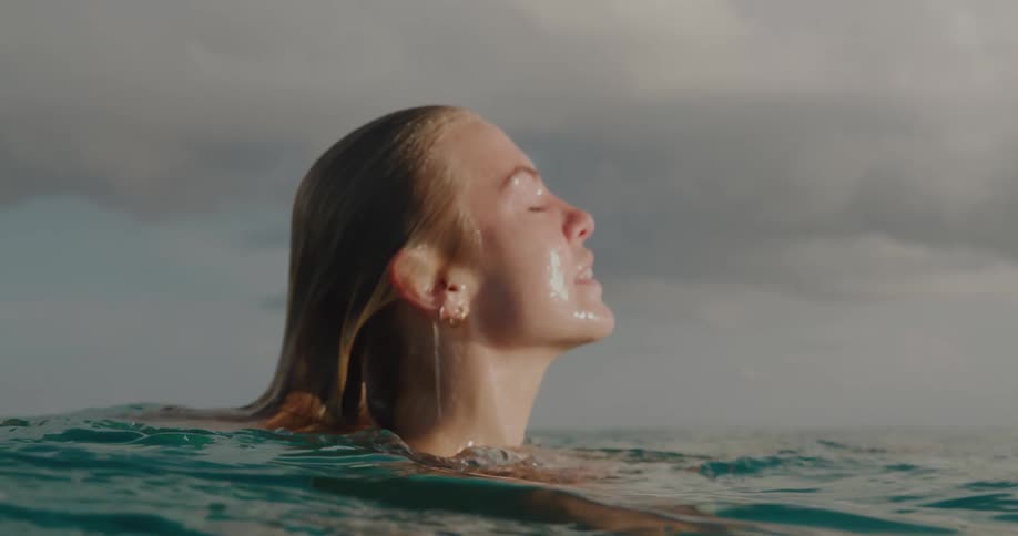 Close up of a woman swimming underwater then coming up to the surface