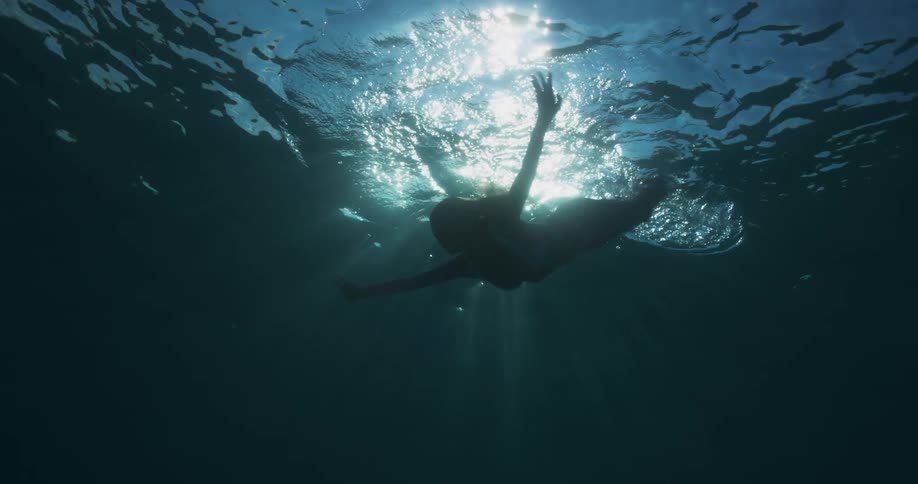 Silhouette of a woman swimming in the ocean against sunlight