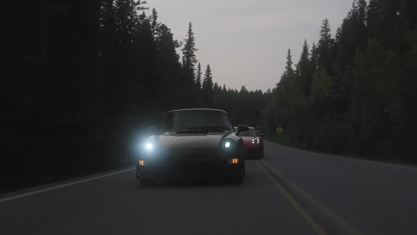 Sports cars traveling on a highway surrounded by trees on a cloudy day