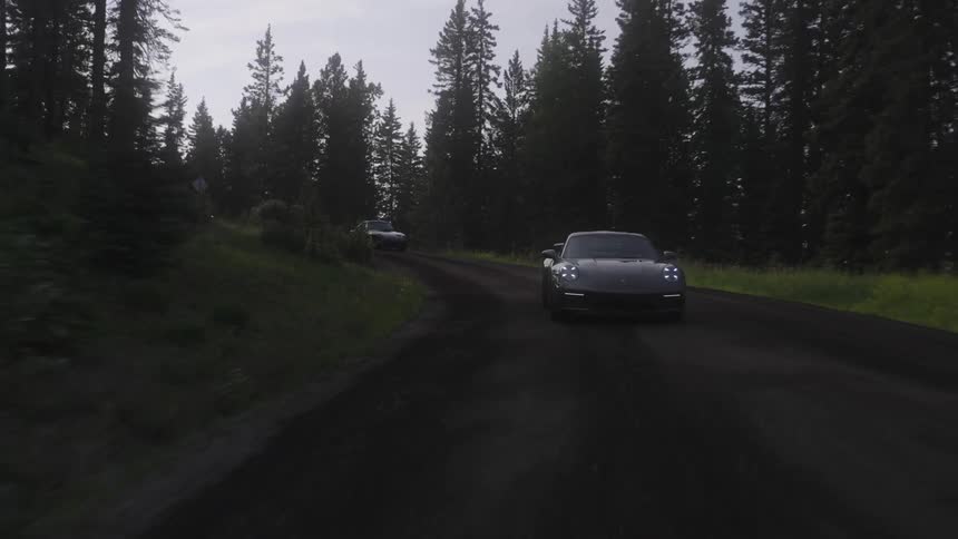 Sports cars traveling along a dirt road with trees around