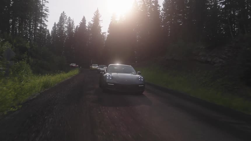 Sports cars traveling along a natural road with trees around