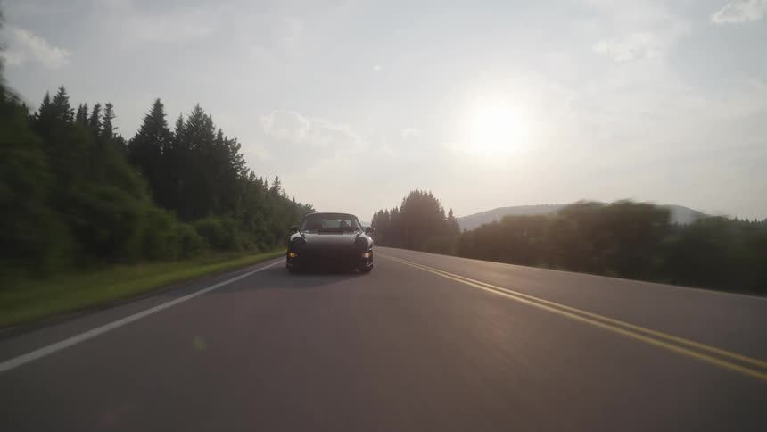 Classic porsche sports cars traveling on a highway with trees around and the sunset on the horizon