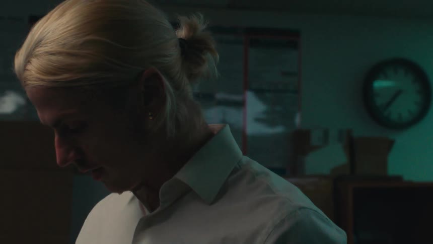 A man with blond hair tied up is picking up something that is in front of him and then looking down