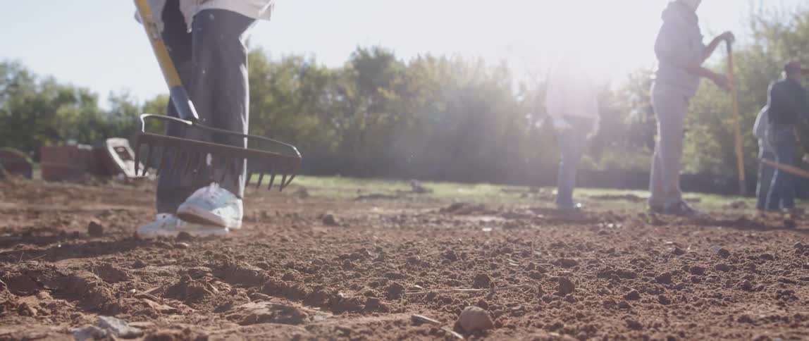A worker rakes dirt in a field during the day