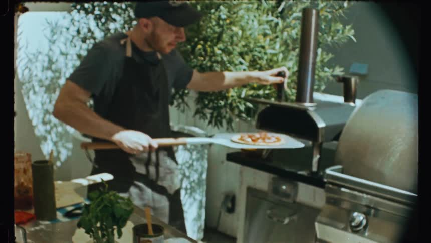 Man taking a baked pizza out of an oven