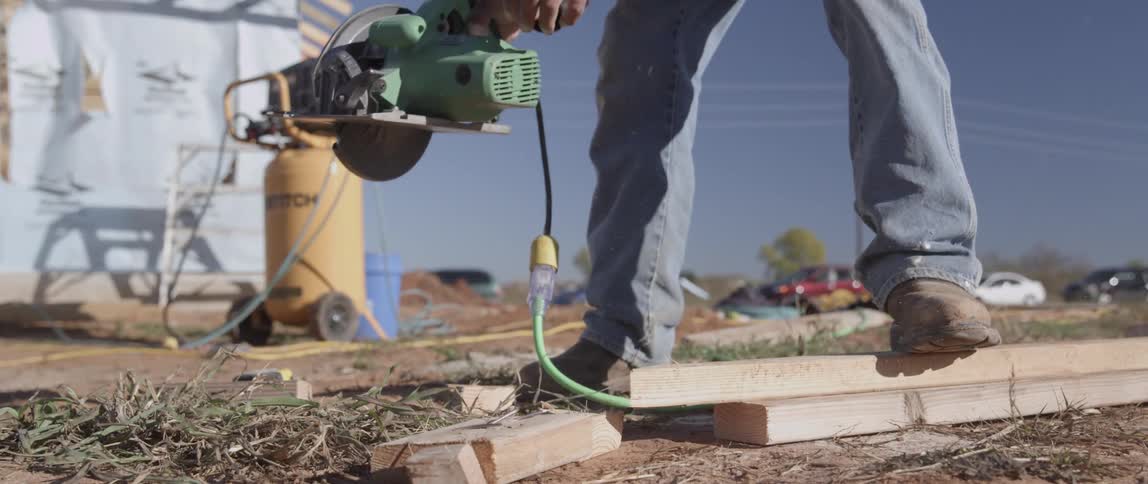 A worker is using a circular saw to cut two by fours outside