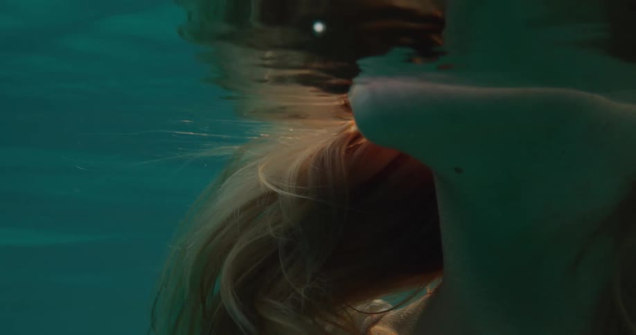 Neck of a lighthaired woman submerged in an ocean with reflections of natural light
