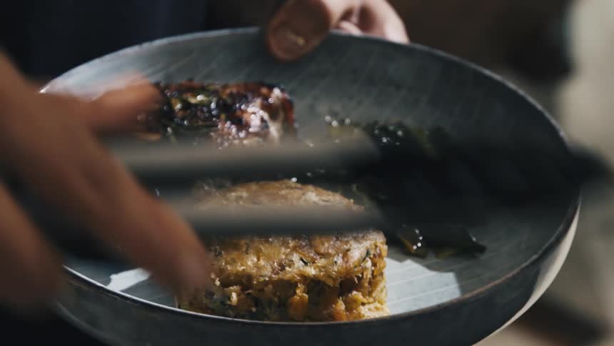 A young chef plates food in a gray bowl