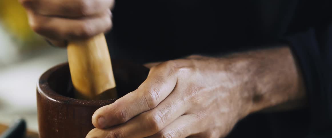 A man is crushing herbs with a mortar and pestle