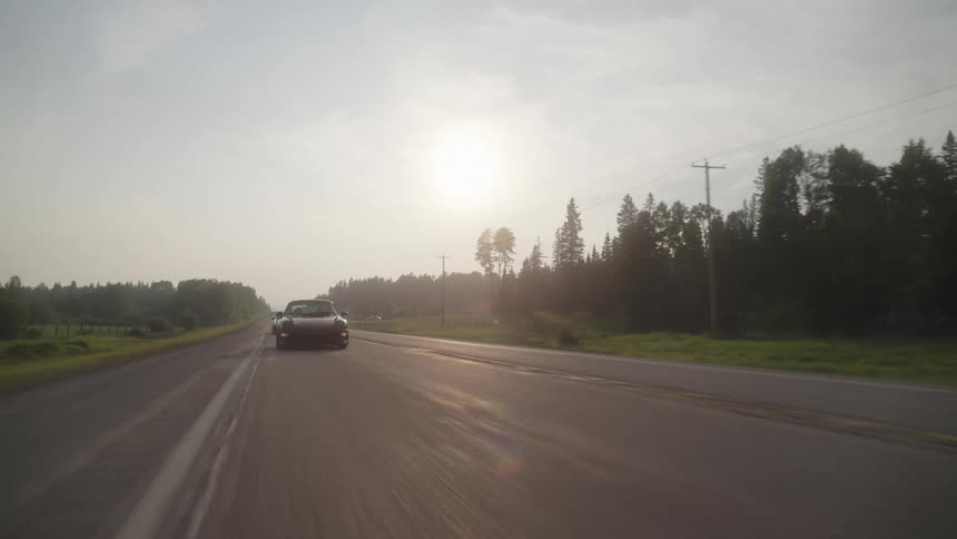 Two sports car drive down a highway next to a forest