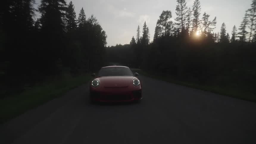 A porsche 911 gt3 drives down a country road at dusk