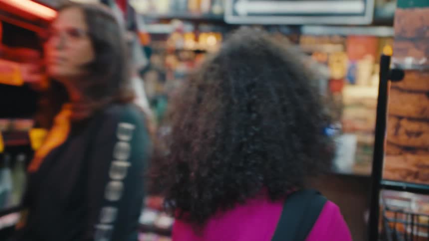 Back view of a curlyhaired woman walking down the aisles of a supermarket